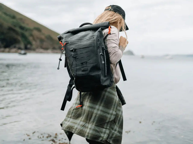 Eine Frau wandert am Strand und traegt den neuen Adventure Waterproof Backpack